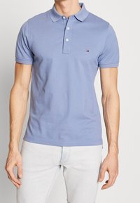 Light blue cotton polo shirt with a collared neckline and three-button placket. Features a small logo on the chest and short sleeves.
