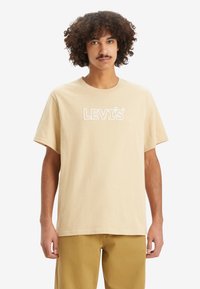 Bež puuvilla T-särk lühikeste varrukatega, ümmargune kaelus ja valge "LEVI'S" logo prinditud ees. Silus tekstuur ja mugav lõige.