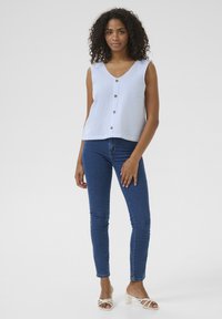 Haut sans manches bleu et blanc à rayures, avec un col en V et des boutons, associé à un jean skinny en denim foncé et des sandales à talons de couleur claire.