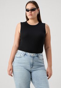 Black ribbed tank top with a round neckline, paired with light blue high-waisted jeans. The model wears black sunglasses and hoop earrings.