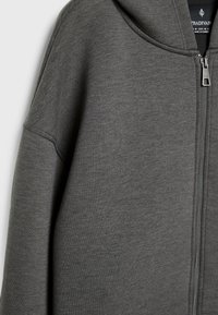 Sweat à capuche gris zippé avec une finition douce et texturée, doté d'une grande capuche et d'un design minimaliste. Légère usure visible sur le tissu.
