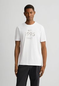 Witte katoenen T-shirt met korte mouwen. De voorkant heeft een textuurprint met "est. 1995 LIU JO" in een contrasterende kleur. Eenvoudig, klassiek ontwerp.