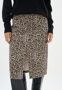 Krilo z leopardjim vzorcem s ravnim krojem, v bež in rjavih odtenkih, z neposredno odprtino spredaj in subtilno teksturo, v kombinaciji s črnima puloverjem.