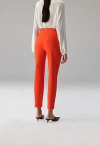 Oranje nauwsluitende broek met een op maat gemaakt silhouet, met een gladde textuur en enkellange zoom, gecombineerd met zwarte mules.