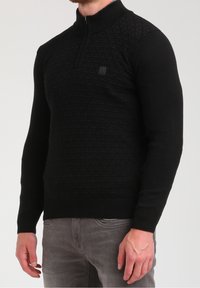 Musta neulepaita vetoketjukauluksella, jossa on tekstuuroitu timanttikuvio edessä ja sileät hihat sekä helma. Kevyt neulottu materiaali.