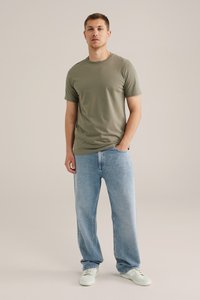 Camiseta de algodón verde oliva de manga corta, combinada con vaqueros de denim de corte holgado en azul claro y zapatillas de color claro.
