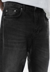 Jeans in denim nero con taglio dritto, dotati di accessori in argento su tasche e una leggera texture sbiadita. Rivetti visibili sulle tasche anteriori.