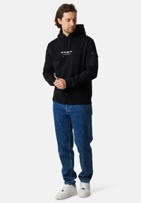 Felpa nera con stampa grafica frontale, tasca a marsupio, cappuccio con cordino, abbinata a jeans blu e sneaker bianche. Tessuto morbido, vestibilità comoda.