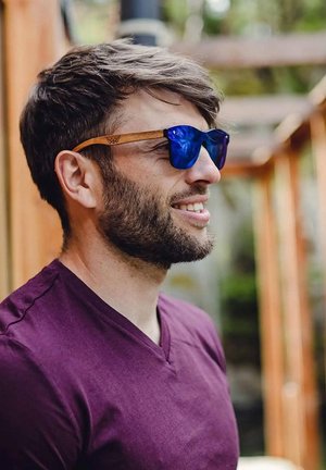 Sluneční brýle s modrými čočkami a dřevěnými obrubami; kulatý tvar, minimalistický design a jemné geometrické vzory na stranách.