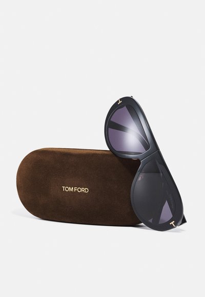 Occhiali da sole neri con lenti scure, caratterizzati da una forma a goccia e dettagli dorati. Accompagnati da una custodia in suede marrone con il marchio "TOM FORD" impresso.