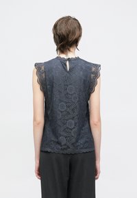 Tumši zils mežģīņu tops ar viļņotām īsām piedurknēm un atveri muguras daļā. Visa virsma rotāta ar smalkiem ziedu un ģeometriskiem rakstiem.