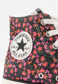 Scarpe Converse alte in tessuto nero con motivo floreale in rosa e verde; presentano una toppa con logo bianco e occhielli in metallo per i lacci.