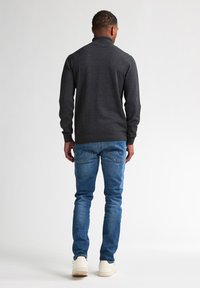 Suéter gris de manga larga con cuello alto, combinado con jeans ajustados azules y zapatillas blancas, visto desde atrás.