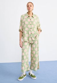 Groen en roze gestreepte tweedelige outfit, bestaande uit een losse blouse met knopen en wijde broekspijpen, gecombineerd met groene sneakers en witte sokken.