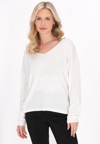 Maglione bianco, leggero, con maniche lunghe a V e polsini e orlo smockati. Vestibilità ampia, tessuto testurizzato, abbinato a pantaloni neri.