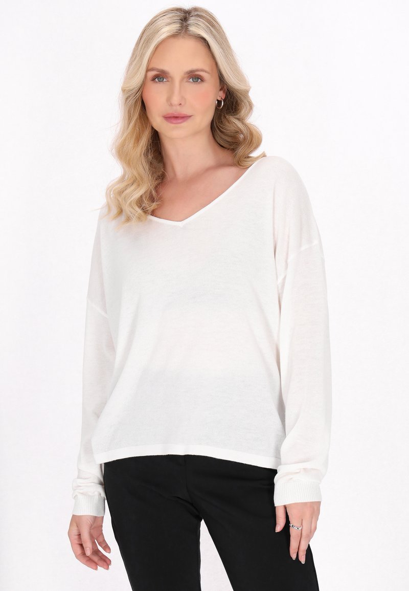 Maglione bianco, leggero, con maniche lunghe a V e polsini e orlo smockati. Vestibilità ampia, tessuto testurizzato, abbinato a pantaloni neri.