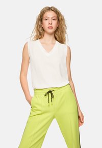 White sleeveless top with a V-neck design paired with bright lime green, textured jogger pants featuring an adjustable drawstring.