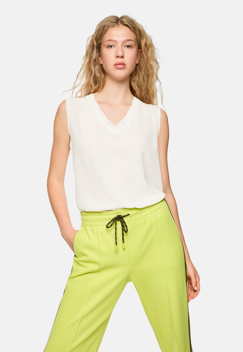 White sleeveless top with a V-neck design paired with bright lime green, textured jogger pants featuring an adjustable drawstring.