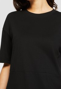 Czarny bawełniany t-shirt o luźnym kroju, z krótkimi rękawami i okrągłym dekoltem. Gładka struktura i minimalne detale przeszycia.