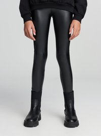 Czarne, błyszczące legginsy wykonane z elastycznego, dopasowanego materiału, zestawione z czarnymi botkami za kostkę z teksturowaną podeszwą i elastycznym mankietem.