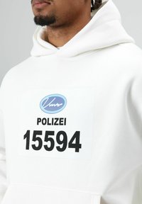 Witte hoodie met een grote rechthoekige patch waarop het woord "POLIZEI" en het nummer "15594" in zwart staan, met daarboven een blauw rond logo.