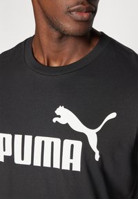 Sort bomulds T-shirt med et fremtrædende hvidt "PUMA" logo og et springende pantergrafik i kontrasterende farver. Rund hals design.