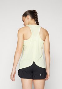Light yellow sleeveless tank top with a gathered back design, paired with black shorts featuring a small white logo. Smooth texture, athletic fit.