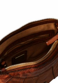 Interior de bolso de cuero marrón con bolsillo con cremallera; textura suave y forrado en tela clara; costuras visibles y cremallera de metal.