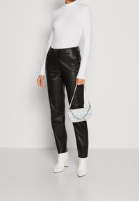 Schwarze Lederhose mit hoher Taille, weißes Langarmoberteil, weiße Blockabsatz-Stiefeletten und eine kleine Handtasche aus blauem Karo mit Kettendetail.