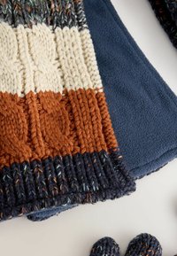 Knit scarf with multi-colored patterns in cream, orange, and navy, featuring a textured cable design. Soft fleece backing. Includes matching gloves.