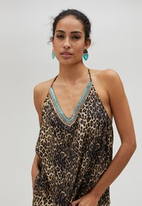 Haut halter à imprimé léopard avec un décolleté en V profond et un col en perles turquoise. Tissu léger, coupe ample et design minimaliste.
