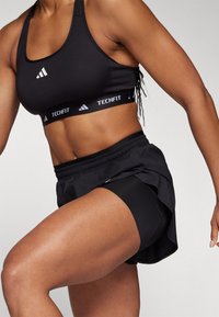 Sort adidas Techfit sports-bh og sorte træningsshorts, der fremhæver et tætsiddende design, strækbart stof og lag-på-lag look med en bred talje.
