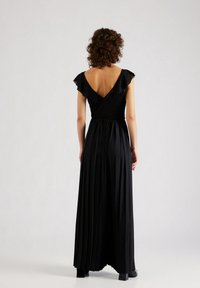 Svart plisserad maxiklänning med V-rygg och flutterärmar. Tillverkad av mjukt tyg med en slät textur, med en figurnära korg och en svävande kjol.