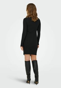 Mustmustriibuline kleit pikkaeiste, vormitud lõikega ja kõrge kaelusega, sobitatud pikkade mustade nahast stilettokontsadega saapadega.