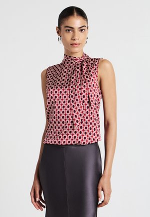 Blouse sans manches rouge avec un col haut et un détail en nœud. Présente un motif circulaire en blanc cassé. Tissu lisse.