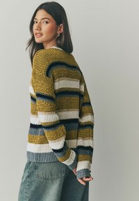 Strickpullover mit kräftigen horizontalen Streifen in Senfgelb, Marineblau und Weiß. Verfügt über ein strukturiertes Gewebe und gerippte Bündchen, kombiniert mit hoch taillierten Jeans.