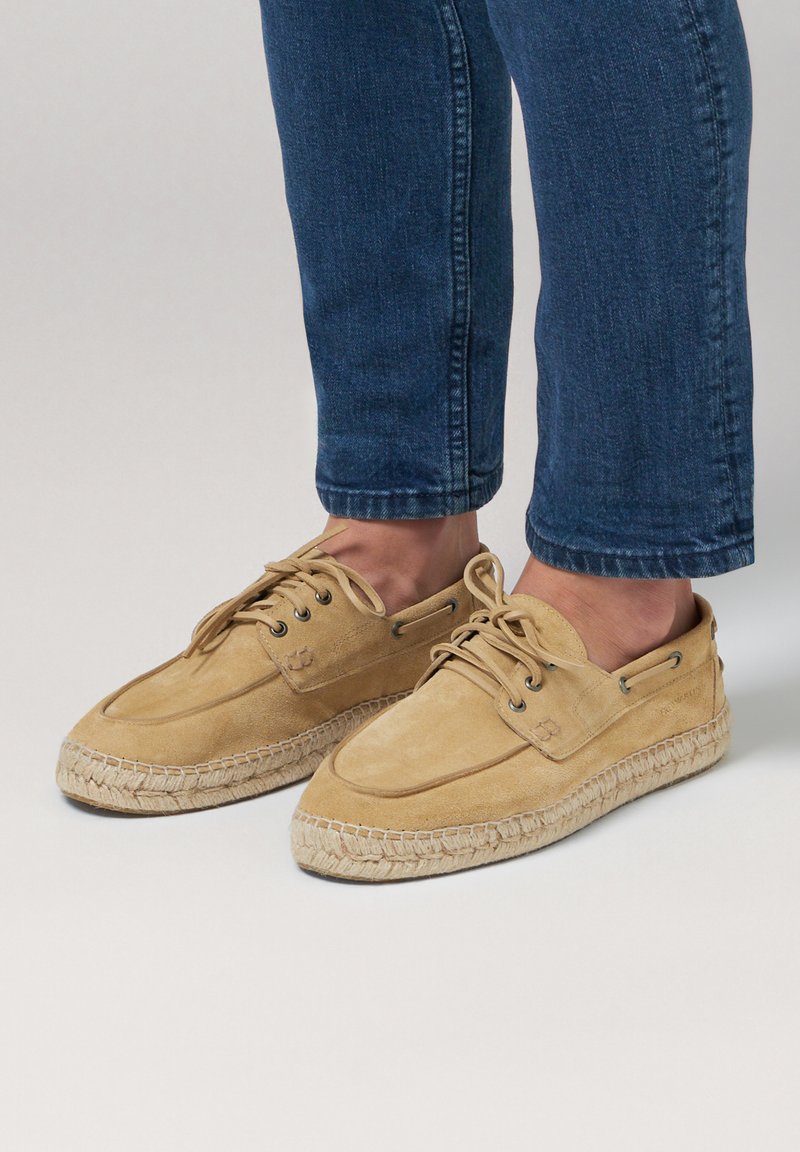 Beige Wildleder-Schnürschuhe mit runder Zehenform, ausgestattet mit einer geflochtenen Jutesohle und gestickten Akzenten. Tragen Sie sie mit hochgeschnittenen blauen Jeans.