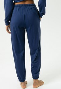 Marineblauwe joggingbroek van zachte stof met een elastische tailleband, taps toelopende pijpen en omgeslagen enkels. Eenvoudig ontwerp met zijzakken.
