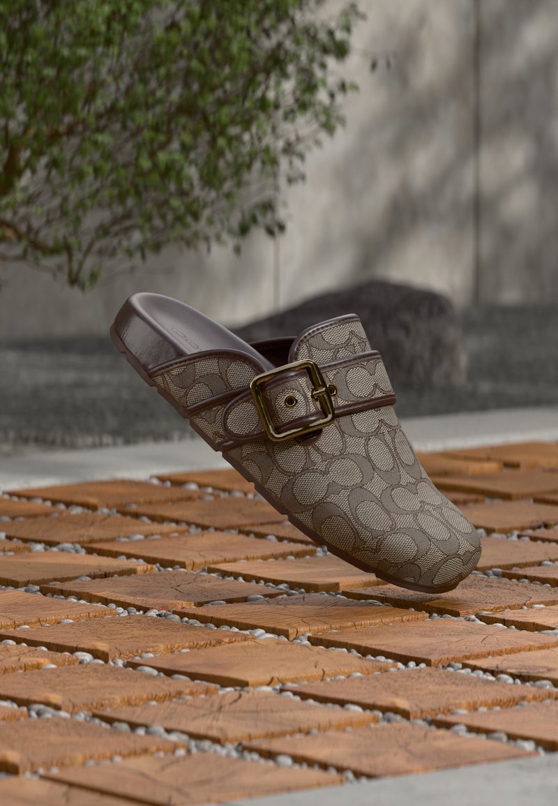 Brun mønstret slip-on sko med bred tåboks, struktureret design og guldfarvet metalspænde på en tekstureret overflade.