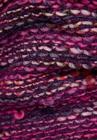 Strickstoff mit einem strukturierten, mehrfarbigen Muster in vorherrschenden Schattierungen von Magenta, Lila sowie Akzenten aus weißen und orangen Fäden.