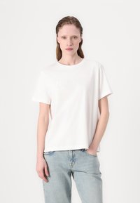 Hvid bomulds T-shirt med korte ærmer, rund halsudskæring, prydet med en tonal præget "GANT" logo på forsiden, parret med lyseblå denim jeans.