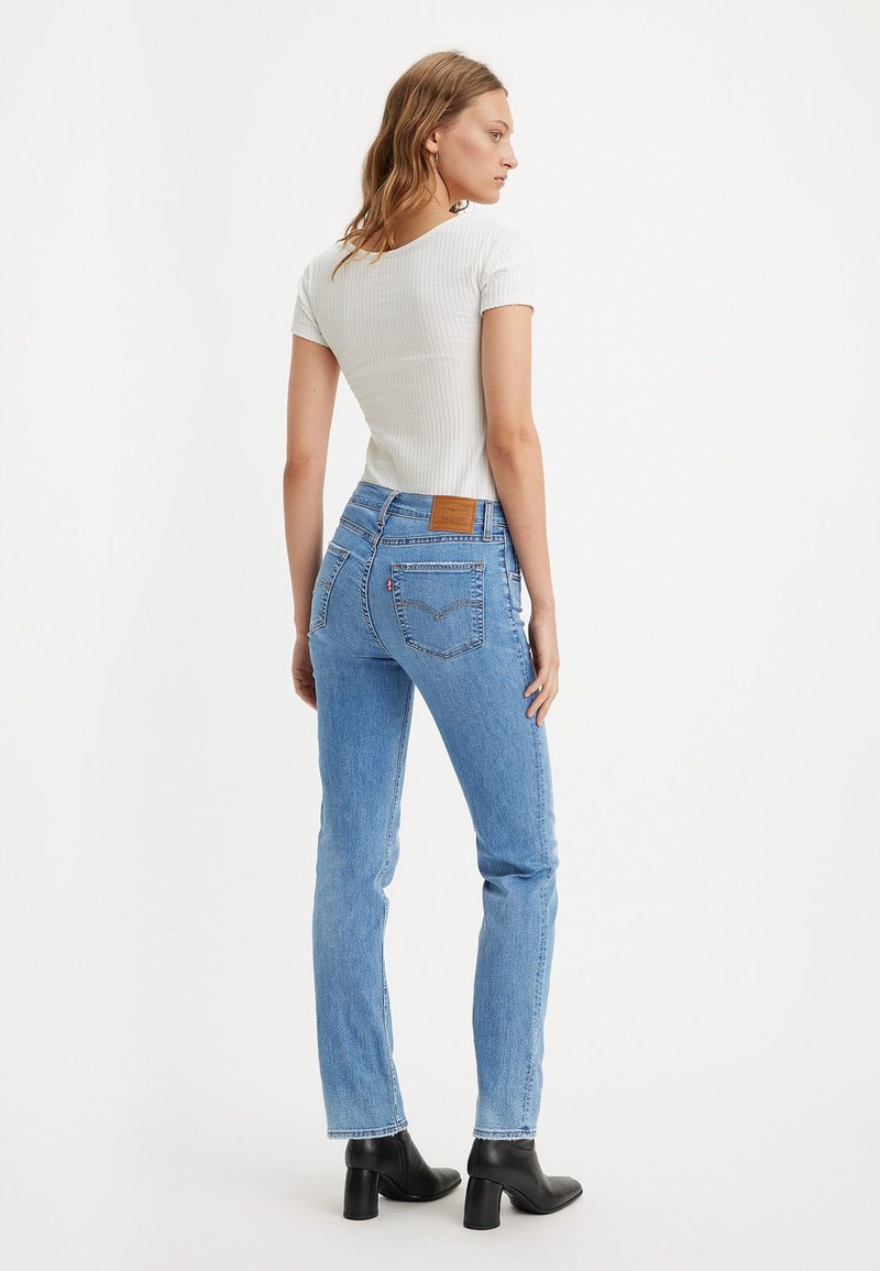 Jean droit bleu clair à taille haute, avec une pièce en cuir au dos et des détails de couture. Assorti avec un haut blanc ajusté en maille côtelée.