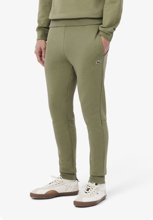 Pantalones de chándal verdes de algodón con un corte slim, bolsillos laterales y un pequeño logo bordado. Combinados con zapatillas blancas con detalles en marrón.