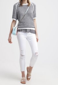 Suéter de punto ligero en blanco y negro, superpuesto a una camiseta gris. Combinado con jeans skinnies blancos con roturas y sandalias de deslizar beige.