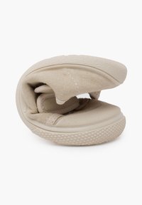 Sneaker beige piegato con tomaia in tela e suola in gomma. Presenta lati testurizzati e una punta liscia, progettato per un facile stoccaggio.
