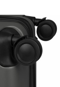 Nahaufnahme von zwei schwarzen Drehrollen, die an der Ecke eines strukturierten, dunkelgrauen Hartschalenkoffers befestigt sind.