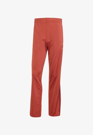 Men's red sports pants made of smooth fabric, featuring an elastic waistband, side slits, and contrasting black accents on the pocket.