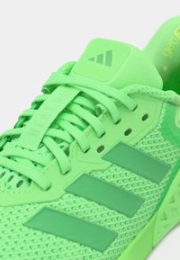 Baskets de sport vertes avec tige en maille, languette rembourrée et trois rayures vert foncé. Elles sont dotées de lacets ajustables et d'accents texturés.