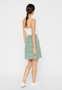 Zelená květinová sukně s úzkým pasem, vrstveným designem a lehkým materiálem. Nosit s bílým tílkem a bílými botami.