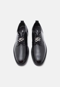 Sapatos de dress de couro preto com um design elegante, bico redondo e um detalhe decorativo de atacador. Textura suave com um acabamento polido.